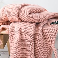 a pink knitted blanket sitting on top of a wooden bench next to a plant