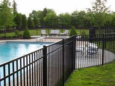 a fenced in pool area with chairs and tables next to the swimming pool, surrounded by lush green grass