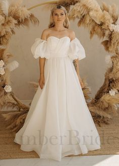 a woman wearing a white dress standing in front of a wreath