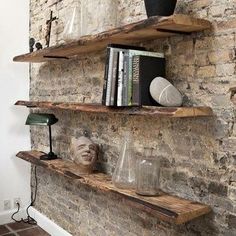 two wooden shelves with books, vases and other items on them in front of a brick wall