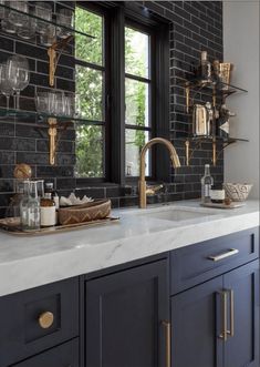 a kitchen with black brick walls and white counter tops, gold pulls on the faucet