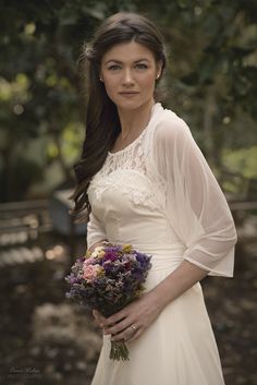 a woman in a white dress holding a bouquet of flowers and looking at the camera