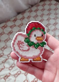 a hand holding a small cross stitch chicken