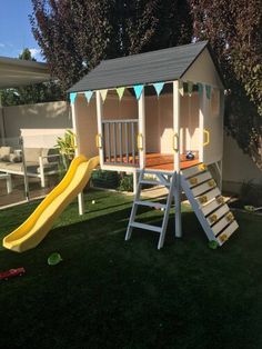 a small wooden play house with a slide in the back yard, and grass surrounding it