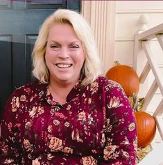 a woman with blonde hair sitting in front of a black door wearing a red floral shirt