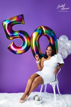 a woman sitting in a chair with balloons and the number 50 on her chest, posing for a photo