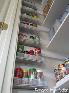 an open refrigerator door with canned food in the bottom shelf and labeled pantry storage below