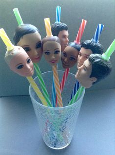 a glass filled with plastic toy heads and drinking straws