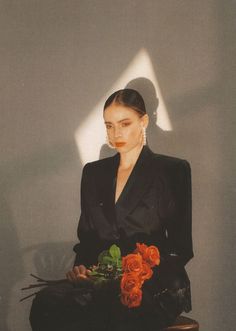 a woman sitting on a chair with flowers in her lap and wearing a black suit