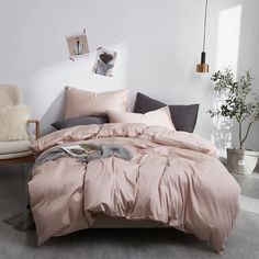 a bed with pink comforter and pillows in a white room next to a chair