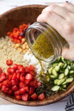 someone pouring dressing into a wooden bowl filled with chopped vegetables and other foodstuffs