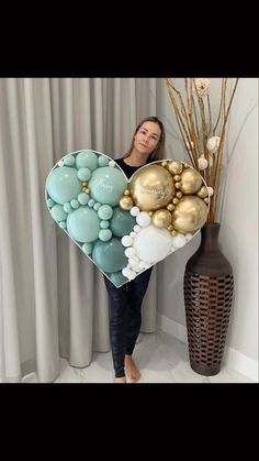 a woman standing next to a vase filled with balloons and balls in the shape of a heart