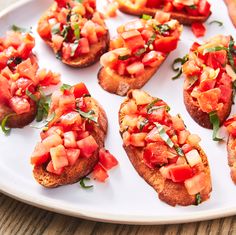 several pieces of bread with tomatoes and basil on them sitting on a white platter