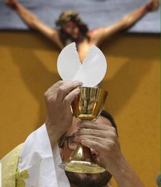 a man holding a chalice in front of his face with the crucifix behind him