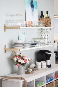 a white shelf filled with glasses and plates on top of a wall next to a vase