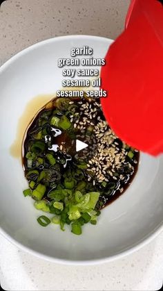 someone is pouring sauce on some food in a white bowl with green peppers and sesame seeds