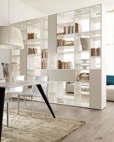 a living room filled with white furniture and bookshelves next to a dining table