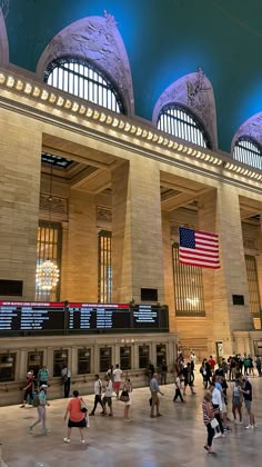 many people are walking around in the train station with american flags hanging from the ceiling