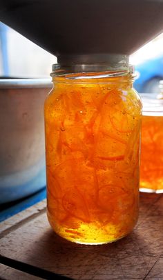 a jar filled with orange liquid sitting on top of a wooden table next to bowls