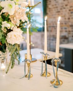 three candles are sitting on a table with flowers and greenery in front of it