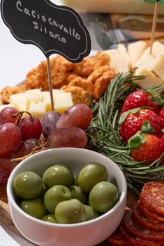 an assortment of cheeses, grapes and meats on a platter with a sign