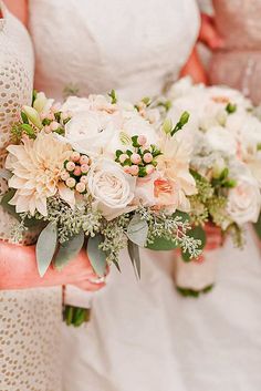 two bridesmaids holding bouquets of white and peach flowers in their hands,