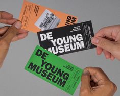 two hands holding tickets with the words de young museum on them and one hand reaching for it