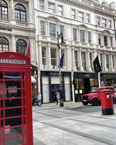 a red phone booth sitting on the side of a road next to tall buildings with windows