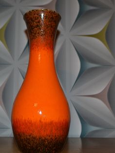 an orange vase sitting on top of a wooden table next to a white and yellow wall