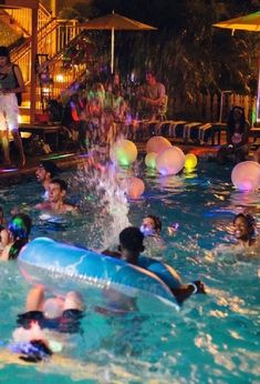 people are playing in the pool at night with water balloons and an inflatable tube