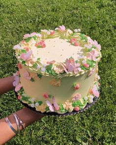 someone is holding a cake with flowers on it in the middle of some green grass