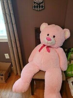 a large pink teddy bear sitting on top of a wooden chair next to a window