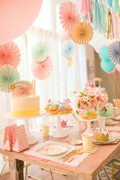 a table topped with cake and cupcakes next to colorful balloons hanging from the ceiling