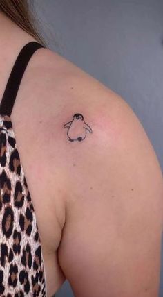 a small penguin tattoo on the back of a woman's shoulder