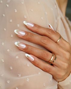 a woman's hand with white nails and gold rings on her left hand, wearing a pink dress