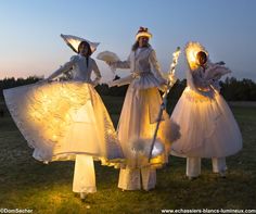 three women dressed in white are standing on the grass with their arms around each other