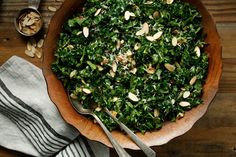 a wooden bowl filled with greens and nuts on top of a table next to two spoons