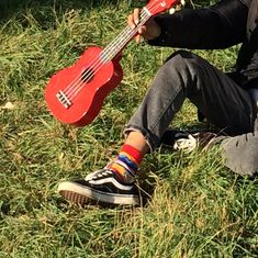 a man sitting in the grass with a red ukulele on his lap and one hand holding it