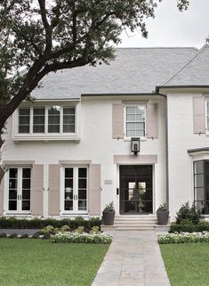 a large white house with lots of windows and plants on the front lawn, along with a walkway leading to it