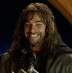 a man with long hair smiling and wearing a leather jacket