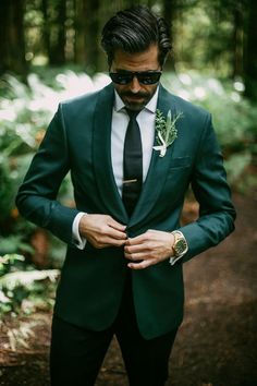 a man in a green suit and sunglasses is looking down at his hand on his lapel