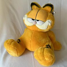 a yellow stuffed animal sitting on top of a white bedding covered sheet with eyes wide open