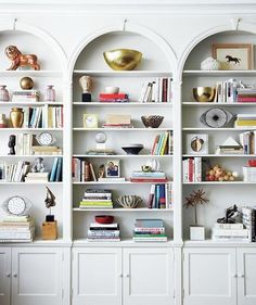 a white bookcase filled with lots of books next to a wall mounted clock and vase