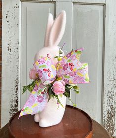 a stuffed rabbit with pink flowers on top of a wooden table next to a white door