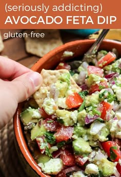 a hand holding a tortilla chip over a bowl of guacamole