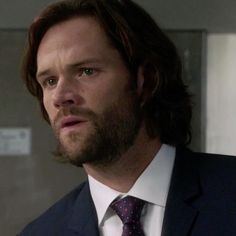 a man with long hair wearing a suit and tie looking off to the side while standing in an elevator