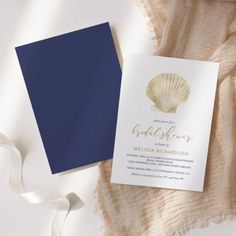 a blue and white wedding card with a seashell on it next to a ribbon