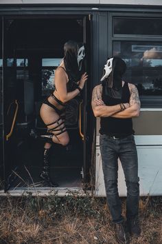 a man and woman wearing masks standing in front of a bus