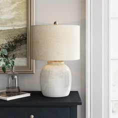 a white vase sitting on top of a black dresser next to a painting and lamp