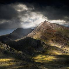 the mountains are covered in green grass and dark clouds